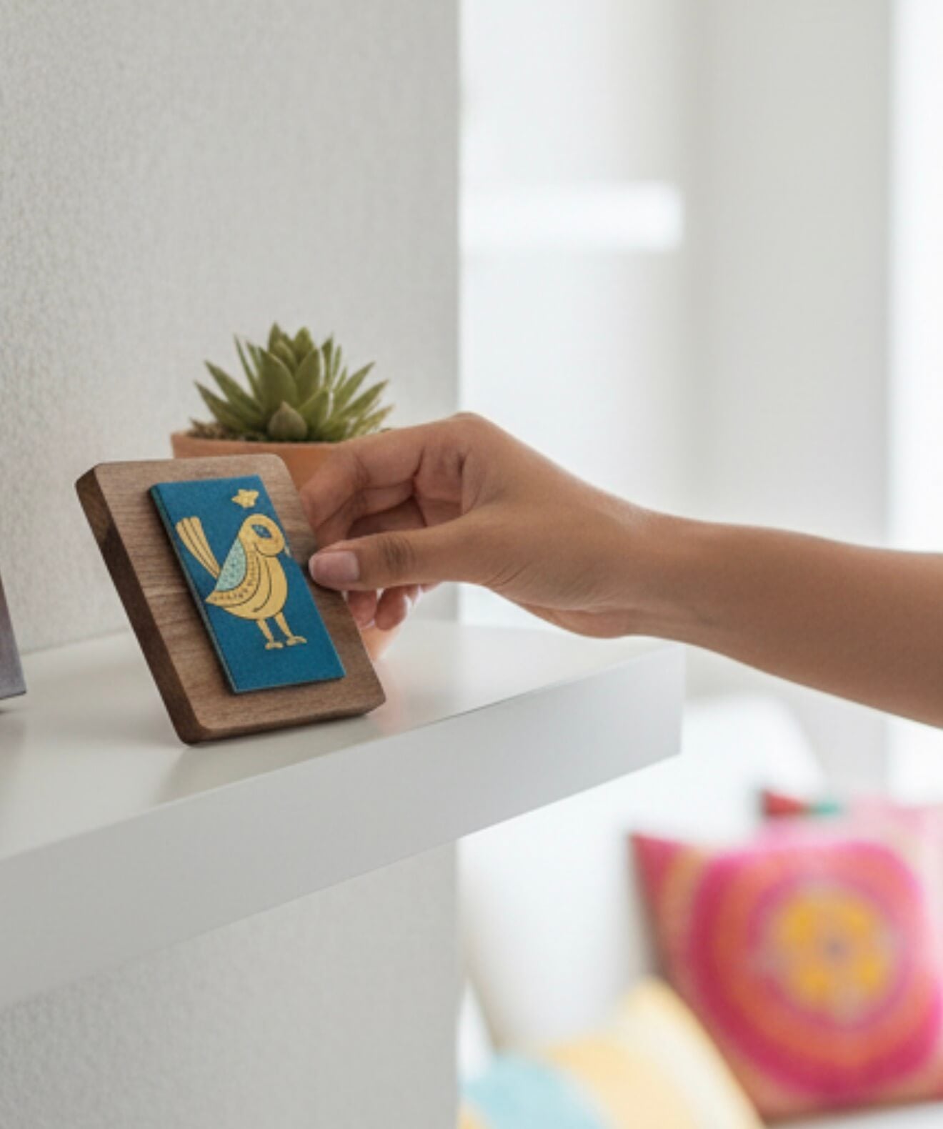 Hand holding a small wooden box with a blue and gold emblem on a white surface.