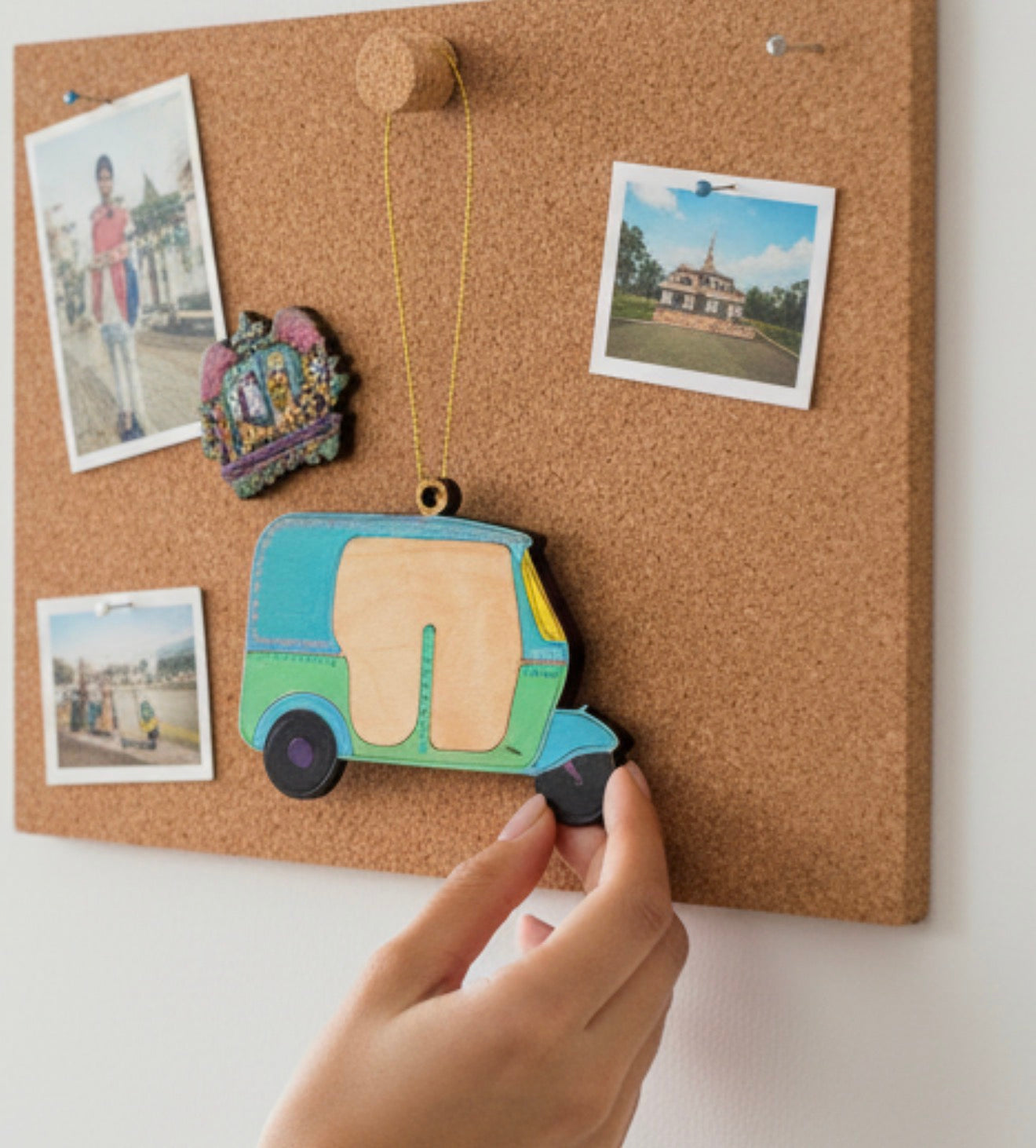 Hand holding a colorful camper-shaped magnet on a cork board with photos
