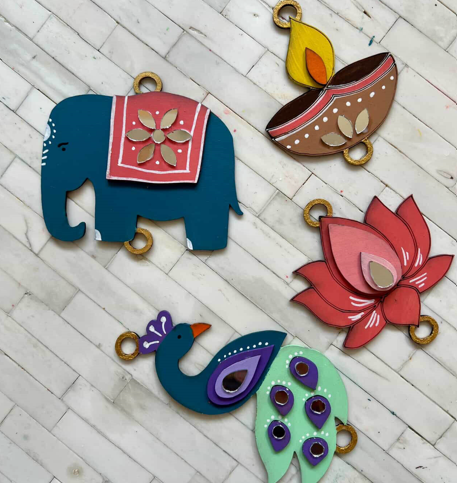 Decorative charms wall hanging including an elephant, lotus, and peacock on a textured white surface.
