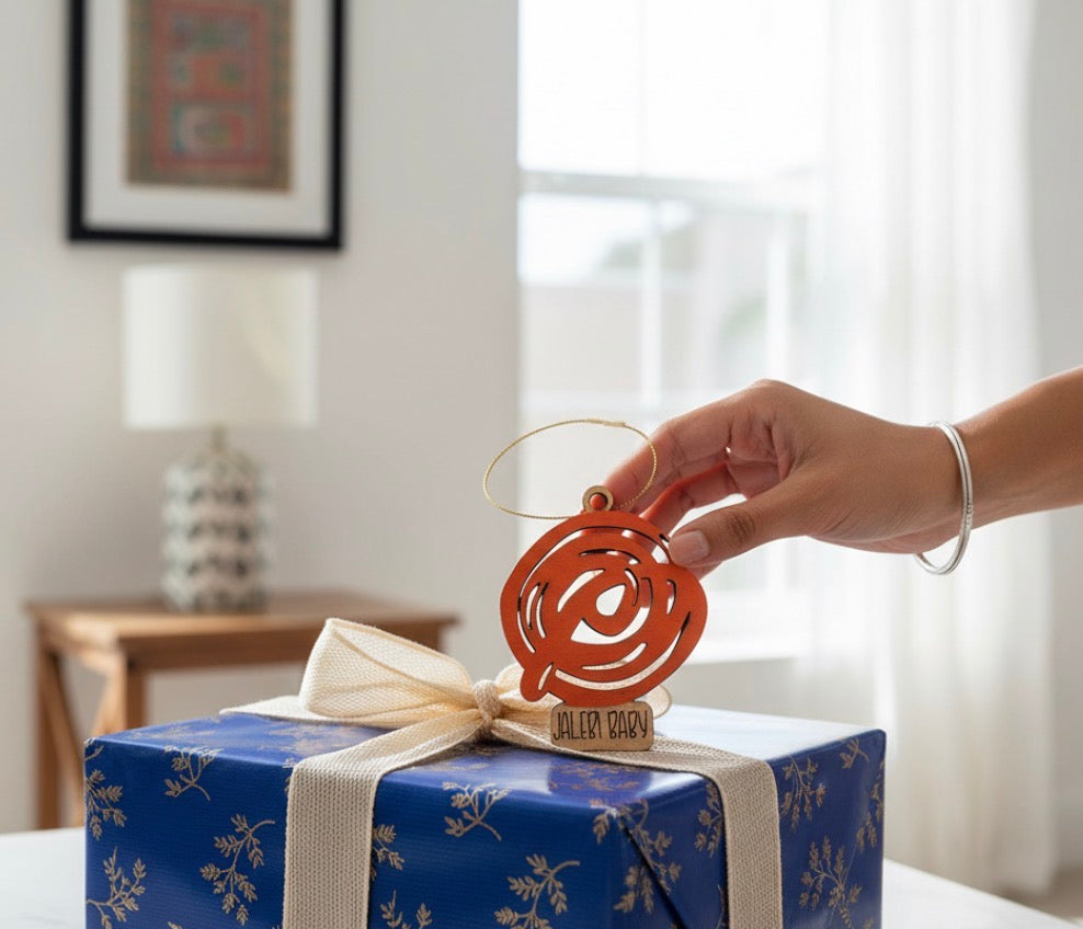 Hand placing a decorative ornament on a wrapped gift with a blue ribbon.