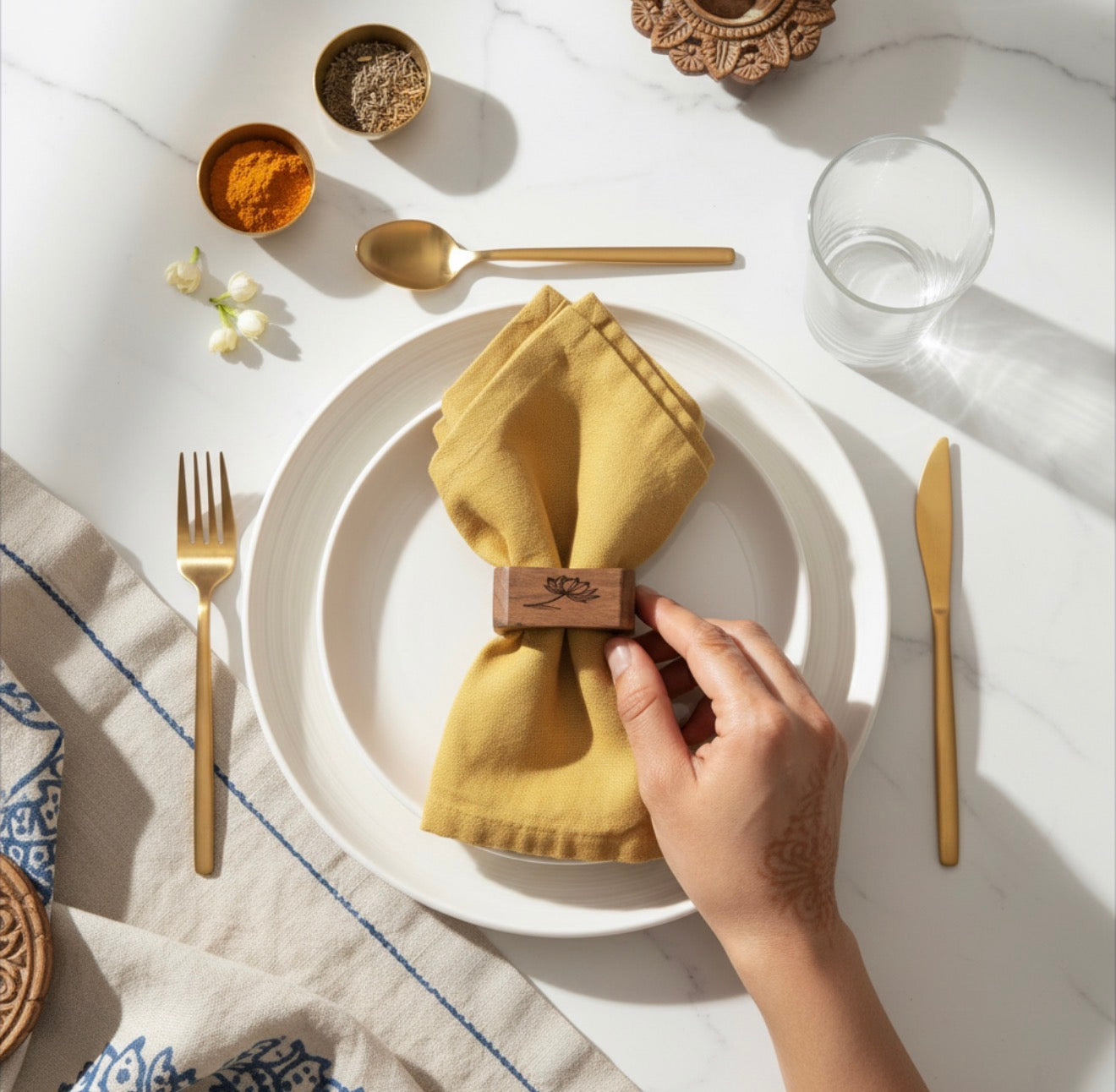 Hand setting a wooden napkin ring on a yellow napkin over a white plate with gold cutlery.