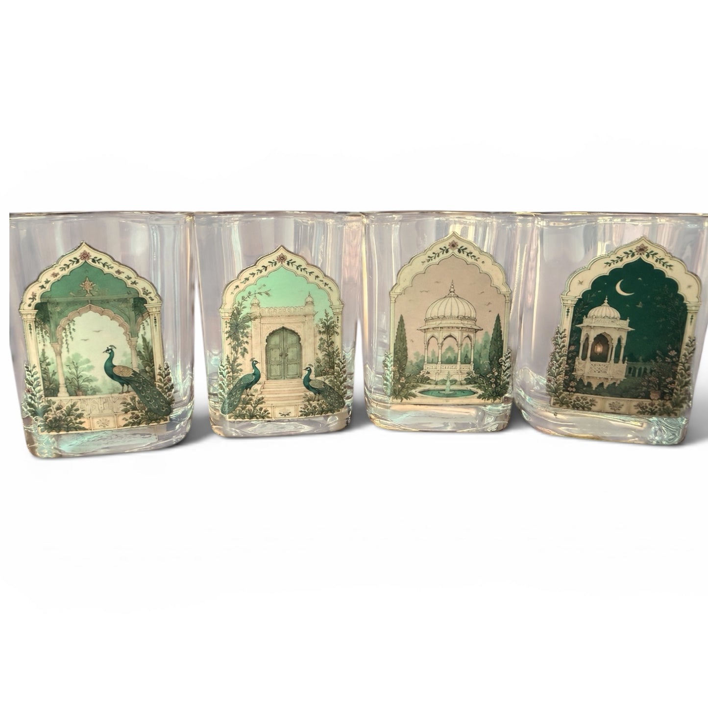 Four clear square drinking glasses with arched printed labels featuring green and beige architectural scenes and peacocks, arranged side by side on a white background.
