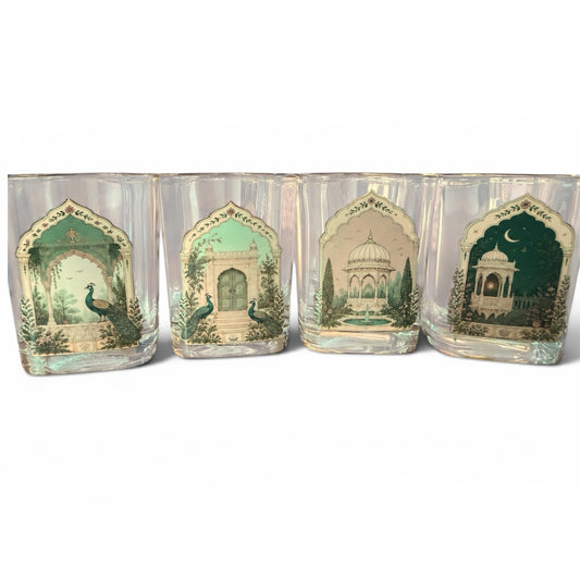 Four clear square drinking glasses with arched printed labels featuring green and beige architectural scenes and peacocks, arranged side by side on a white background.