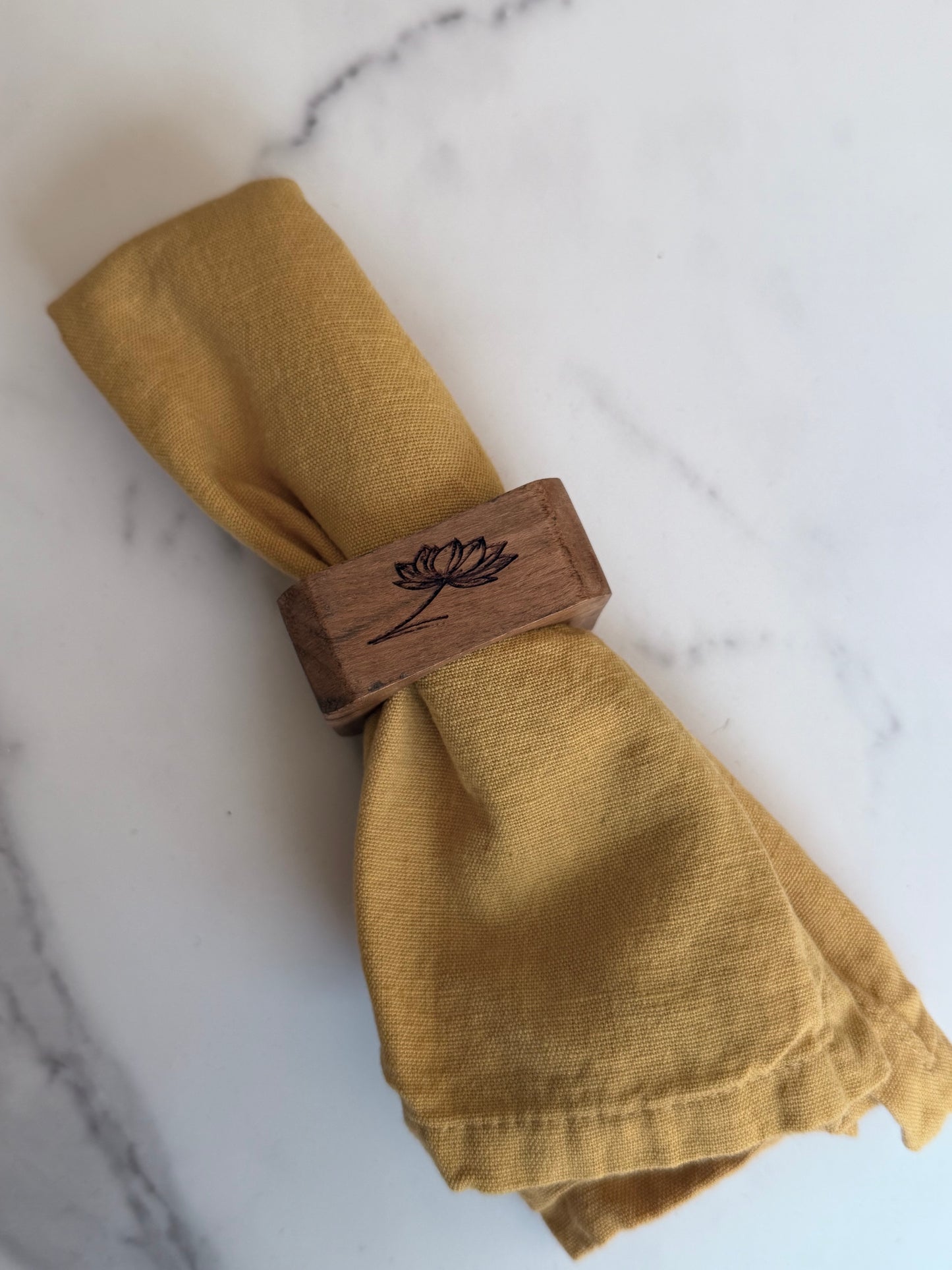 Mustard yellow napkin with wooden napkin ring on a marble surface