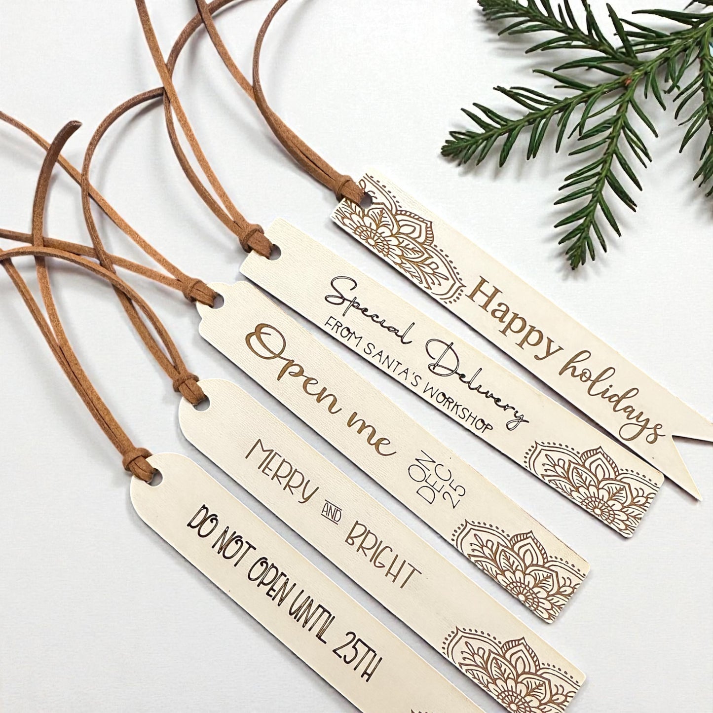 Wooden gift tags with festive messages and decorative designs on a white background with greenery.